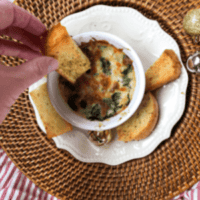 spinach artichoke dip in dish with fingers holding crusty bread