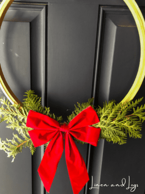 embroidery hoop wreath with cedar branches + red bow on black door