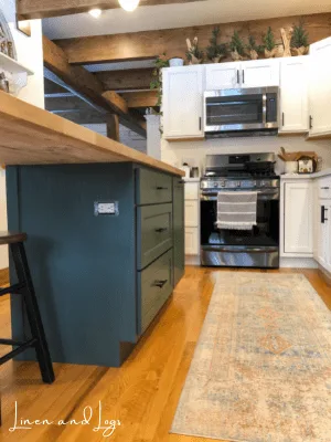 dark green kitchen island with butcher block counter with white cabinets and white counters in a kitchen