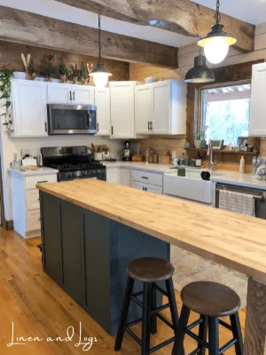 green kitchen island with wood countertop in a rustic kitchen with white cabinets and white countertops