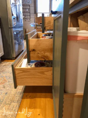 open garbage cabinet and drawers on dark green kitchen island cabinet