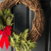 grapevine wreath with cedar branches and red bow on black door