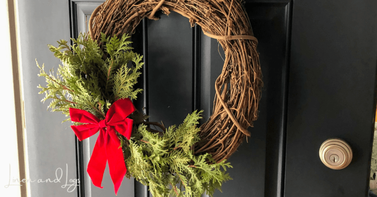 grapevine wreath with cedar branches and red bow on black door