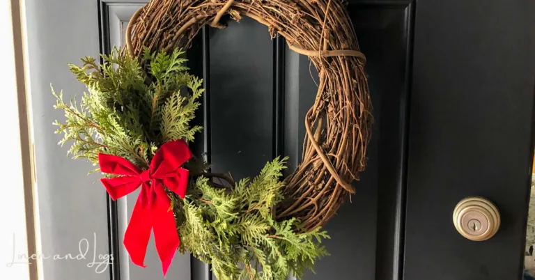 grapevine wreath with cedar branches and red bow on black door