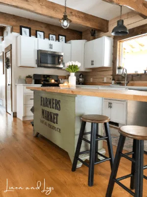 green kitchen island with words stenciled on back in a white kitchen cabinets with wood countertop