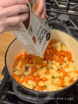 adding beef broth to stew pot with carrots and potatoes