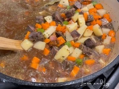 stirring pot of beef stew with carrots, potatoes, bacon