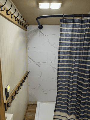 RV Shower with interlocking tile shower walls and hooks on wall with blue shower curtain