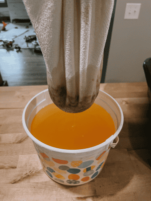 Filtering beef tallow through a flour sack towel into a bucket.