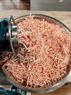 Grinding beef suet into a large metal bowl to render into beef tallow